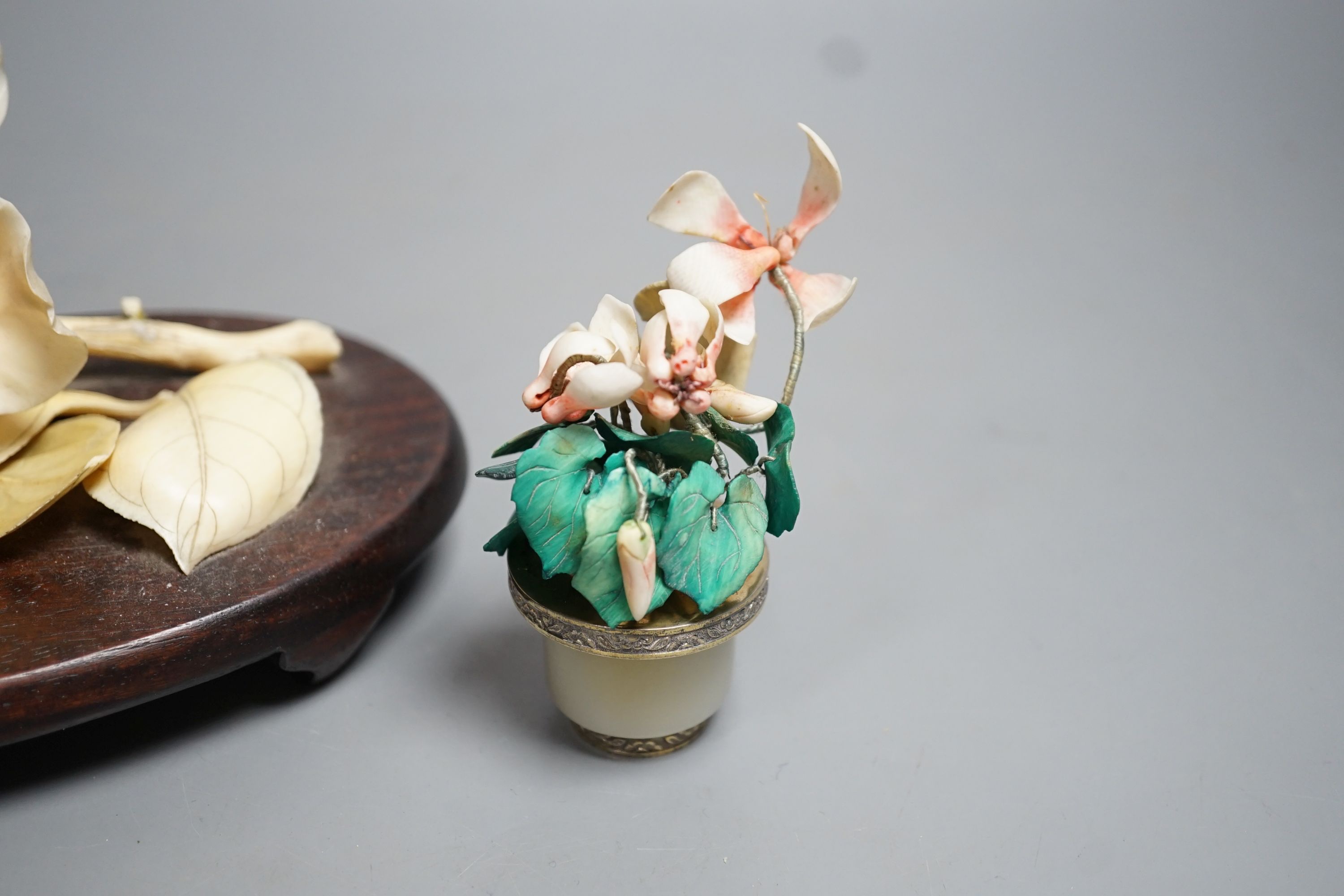 A Chinese ivory model of a peony flower on stand and a Chinese coloured ivory model of flowers with a white jade and white metal plant pot, first half 20th century. Largest measurement 19cm